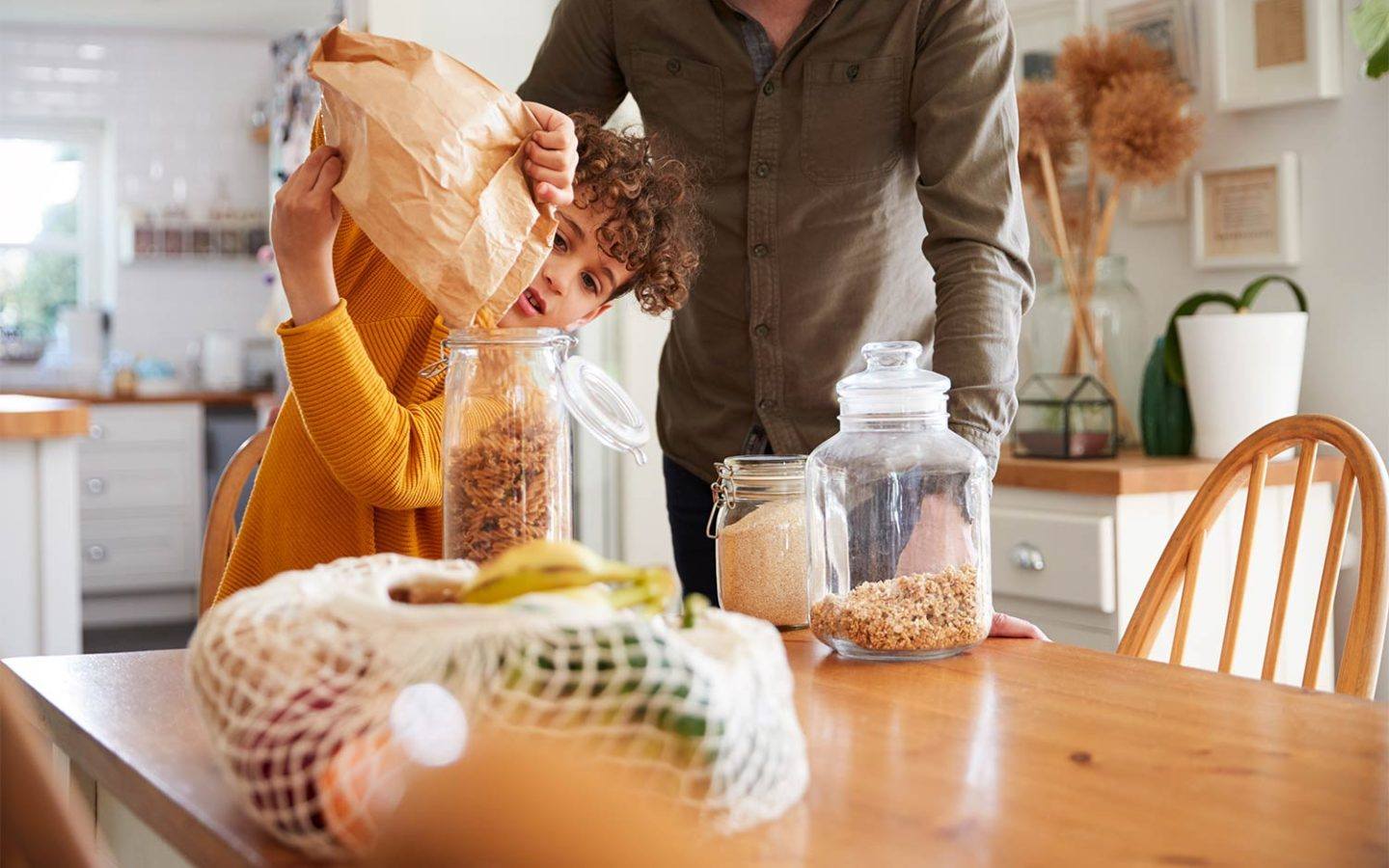 father and young son pour pasta noodles into glass jar to store.